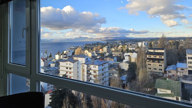 A view from a window overlooking a coastal town with buildings, trees, and mountains in the distance. - Calm Sunrise Bariloche (San Carlos de Bariloche)