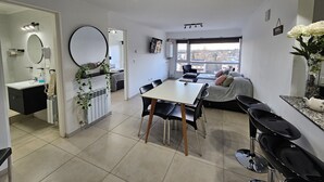 A modern living space with a dining area, kitchen, and a large window offering a city view. - Calm Sunrise Bariloche (San Carlos de Bariloche)