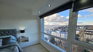 A bedroom with a large window, a bed, a bedside table, and a view of a cityscape. - Calm Sunrise Bariloche (San Carlos de Bariloche)