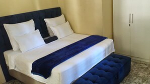 Ein ordentlich bezogenes Bett mit blauer Bettdecke und Kissen, ein dunkles Kopfteil und eine blau gepolsterte Sitzbank am Fußende des Bettes.