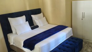 Ein ordentlich bezogenes Bett mit weißer und blauer Bettwäsche, einem dunklen Kopfteil und einer blauen Bank am Fußende.