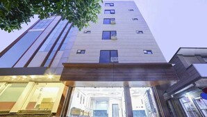 Un hôtel à plusieurs étages, doté d’un design moderne, avec une entrée imposante caractérisée par une façade en verre et un escalier menant au hall d’entrée.