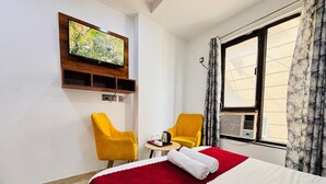 Une chambre d’hôtel avec un lit, deux chaises jaunes, un téléviseur fixé au mur et une fenêtre avec des rideaux.