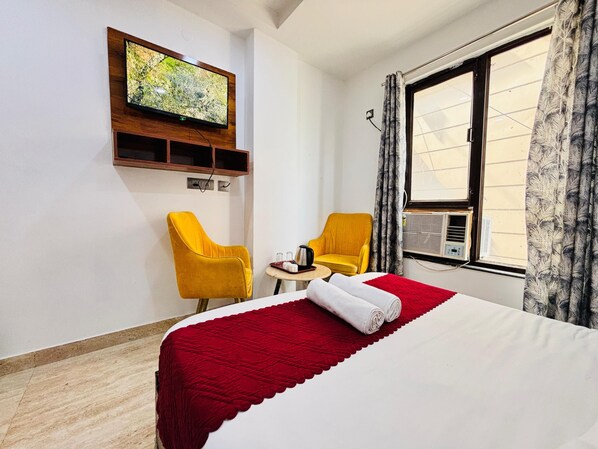 A hotel room with a bed, two yellow chairs, a TV mounted on the wall, and a window with curtains. - Hotel Soho 62 (Noida)