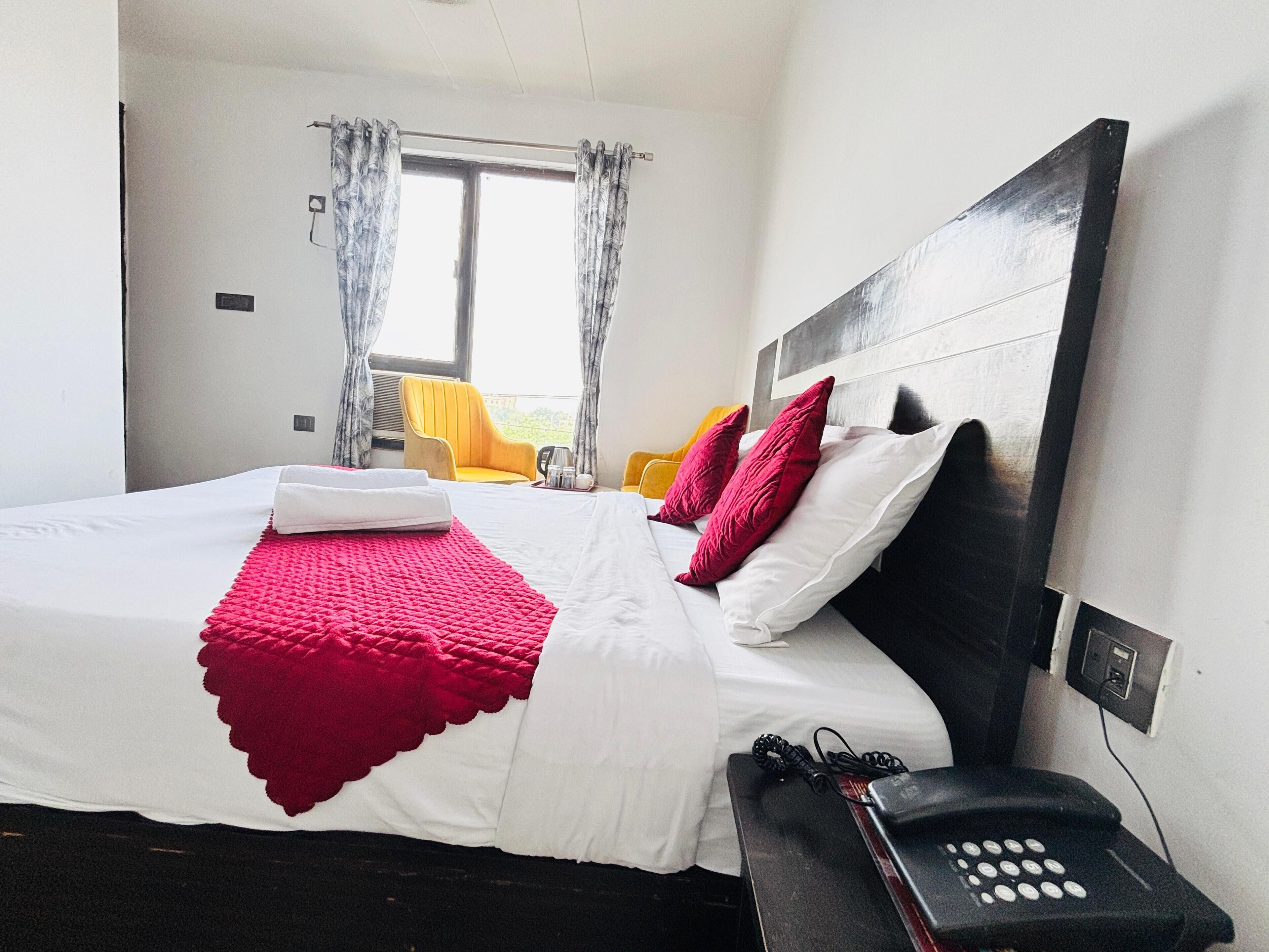 A hotel room with a bed, a bedside telephone, and a window with curtains.