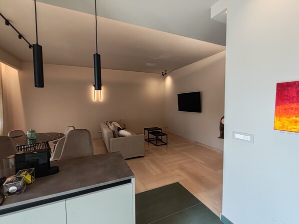 A modern living room with a sofa, a dining table, and a TV mounted on the wall.