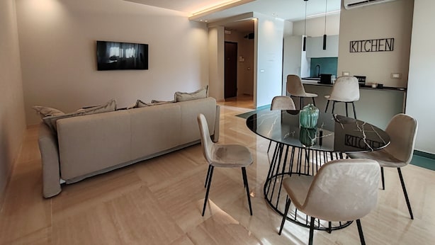 Ein modernes Wohnzimmer mit einer Couch, einem Esstisch mit Stühlen, einem Flachbildfernseher und einer Küchenzeile mit einem Schild, auf dem 'KÜCHE' steht.
