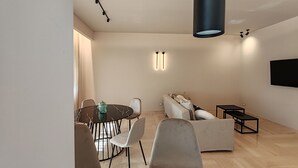 Ein modernes Wohnzimmer mit einem runden Esstisch, zwei Sofas, einem Couchtisch und einem flachbildfernseher an der Wand.