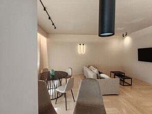 Un soggiorno moderno con un tavolo da pranzo rotondo, due divani, un tavolino da caffè e un televisore a schermo piatto fissato al muro.
