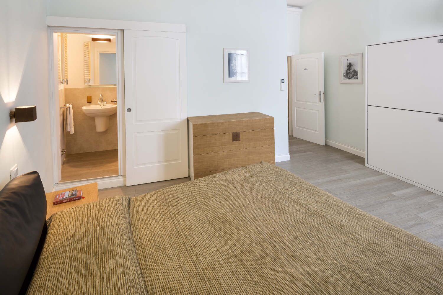 A bedroom with a bed, a wooden chest, a wardrobe, and a bathroom visible through an open door.