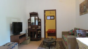 Een woonkamer met een televisie, een houten kast met spiegel, een bank en een kleine tafel met een schaal.