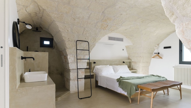 Ein Schlafzimmer mit Steindecke, einem Bett, einem Nachttisch, einer Bank und einem kleinen Fenster.