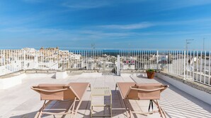 Eine Dachterrasse mit zwei Loungestühlen und einem Tisch mit Blick auf eine Küstenstadt.