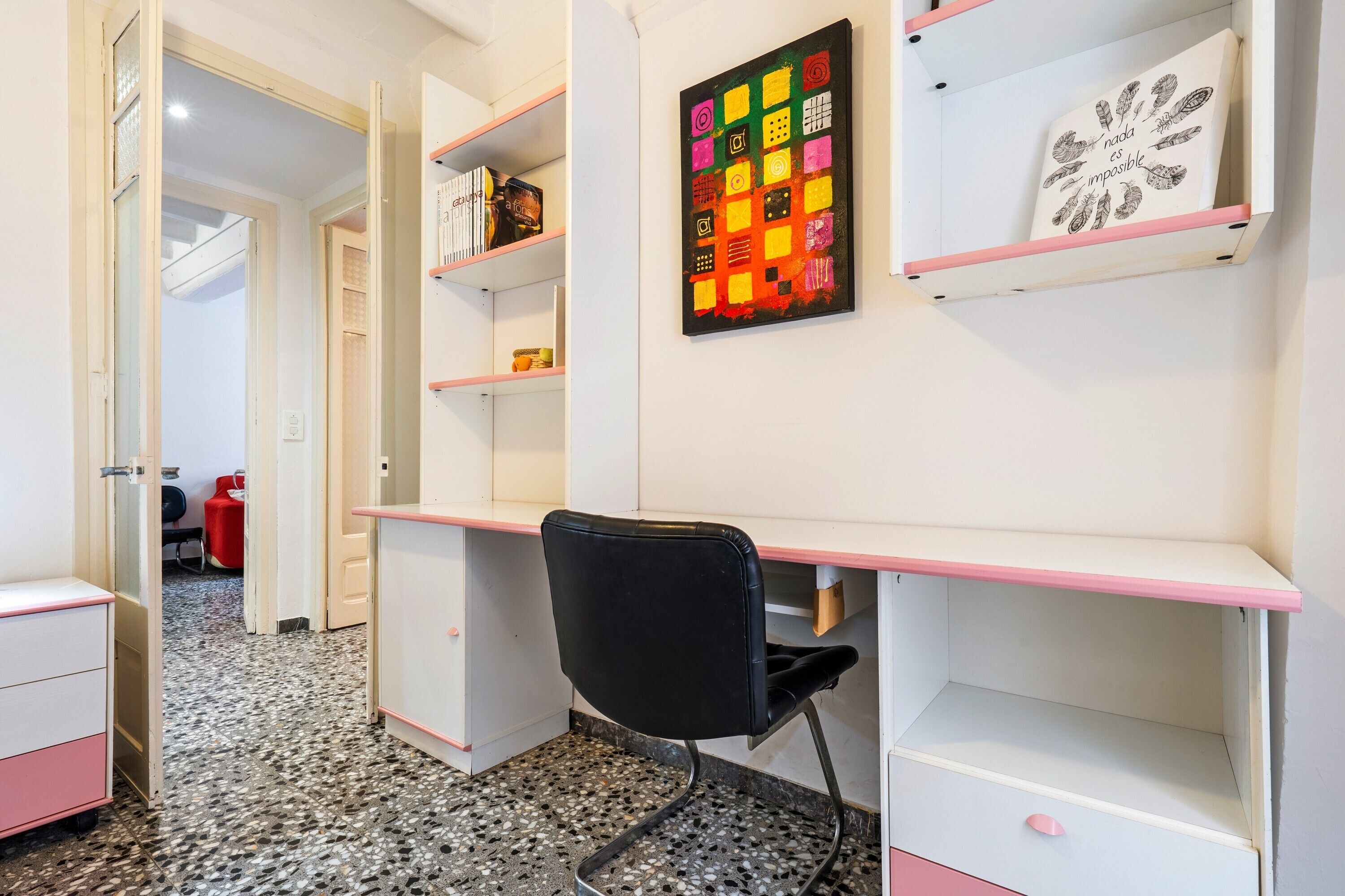 Une pièce comprenant un bureau, des étagères, une chaise et une œuvre d’art murale.