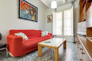 Uma sala de estar com um sofá vermelho, uma mesa de centro de madeira, uma televisão e um quadro na parede.