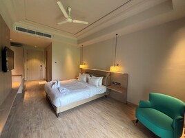 Una habitación de hotel con una cama, un sillón verde, un ventilador de techo y un televisor en la pared.