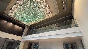 Un vestíbulo espacioso con techo alto, un candelabro decorativo, barandilla de vidrio y una recepción con el letrero "The Supreme Hotel & Restaurant".