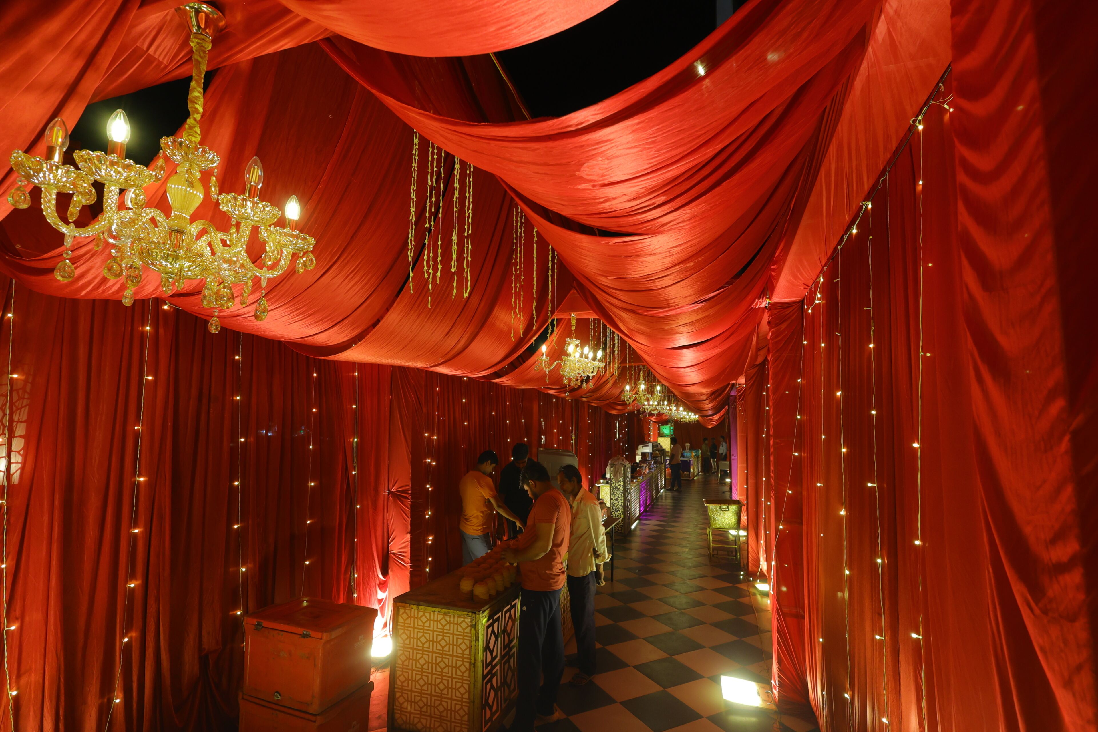 A corridor with draped red fabric, a chandelier, and a checkered floor.