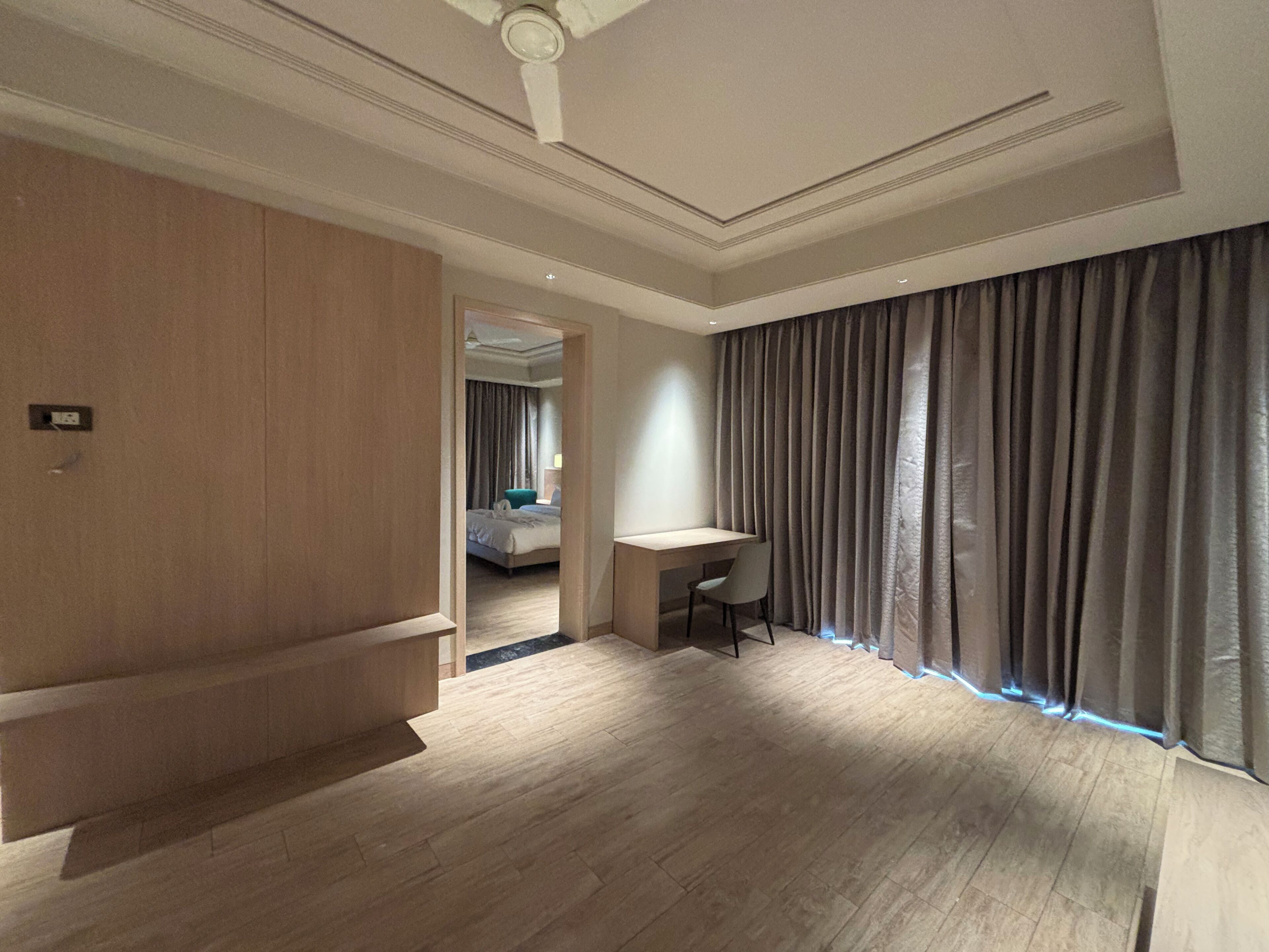 A modern hotel room with a wooden wardrobe, a desk, and a large window with curtains.
