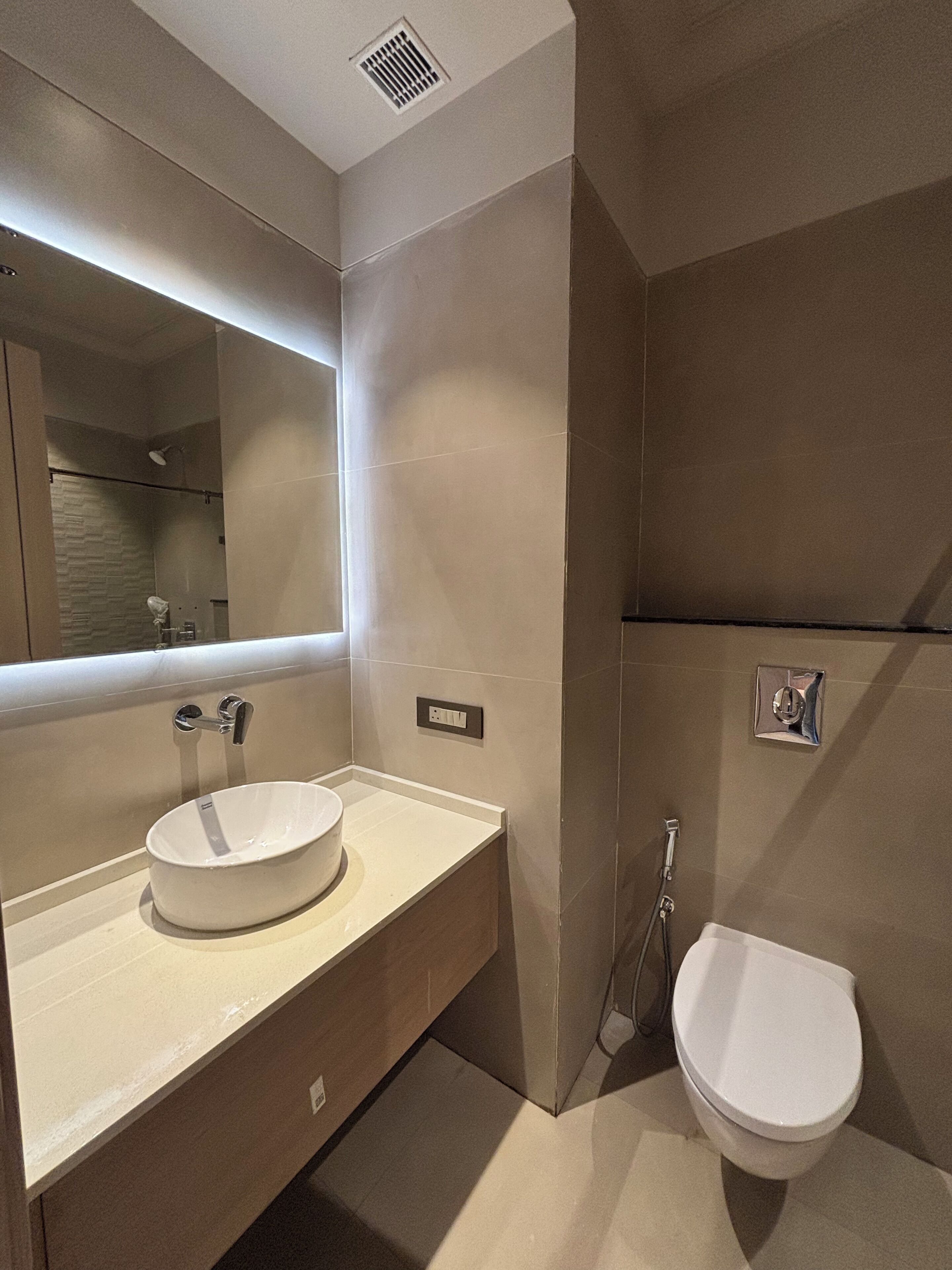 A modern bathroom with a large mirror, a white sink, and a toilet.