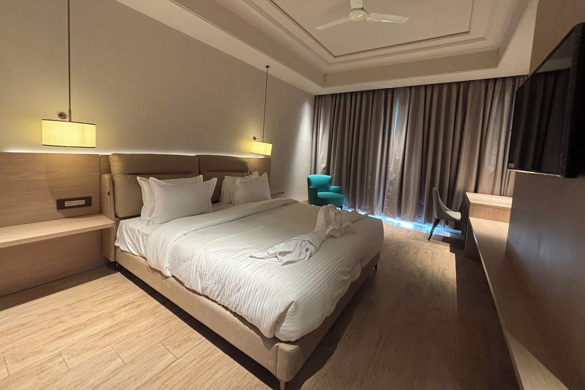 A hotel room with a large bed, bedside tables, a ceiling fan, a TV, and a window with curtains.