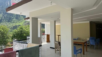 A room with a balcony overlooking a mountainous landscape, a dining area with blue chairs, and a table.