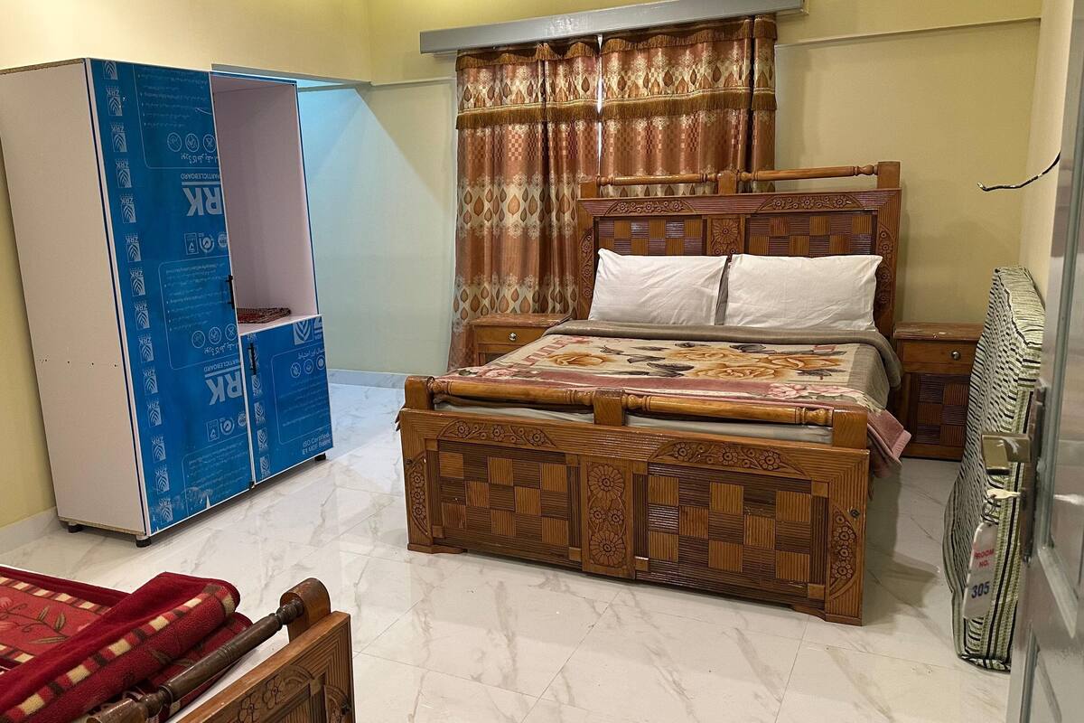 A bedroom with a wooden bed, a wardrobe, a red blanket, and a curtain.