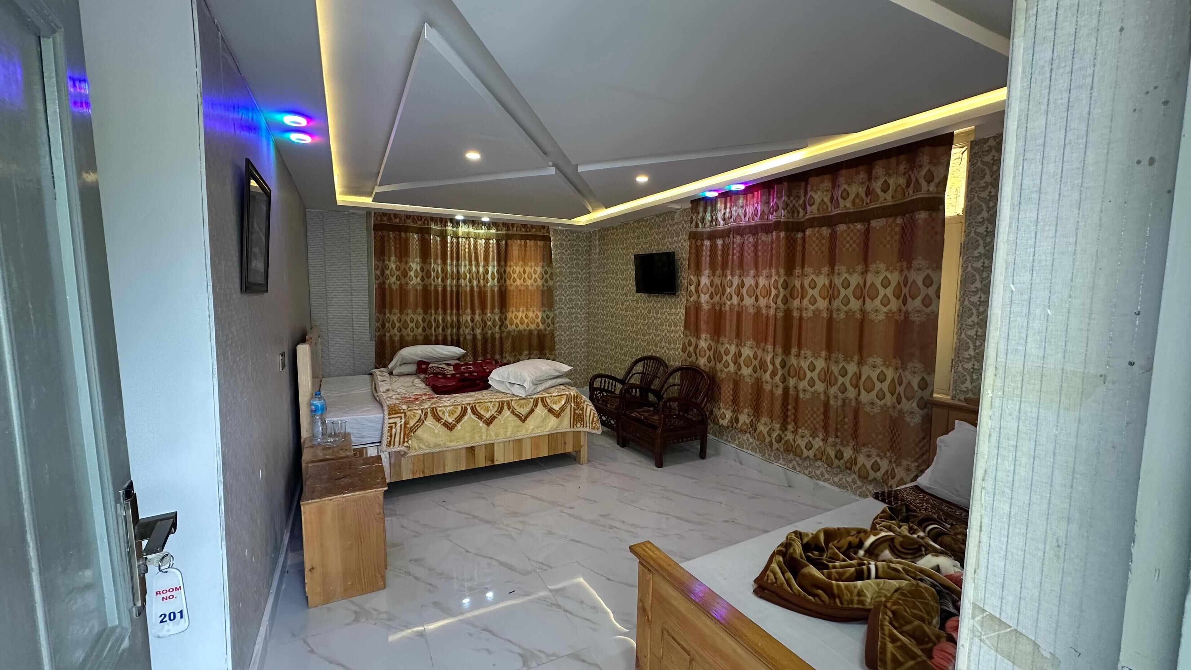 Um quarto com uma cama, uma mesinha, uma cadeira e uma televisão na parede.
