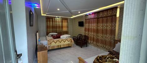 A bedroom with a bed, a small table, a chair, and a TV on the wall.