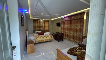 Un dormitorio con cama, una mesita, una silla y un televisor en la pared.