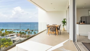 A balcony with a view of the ocean, a dining area with chairs and a table, and a kitchen area. - Penthouse with ocean view / beach access at Mambo Beach (willemstad)