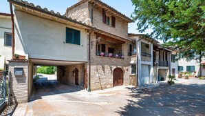 A traditional stone building with a covered entrance, a balcony with potted plants, and a small courtyard.