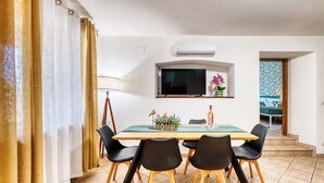 A dining area with a wooden table, black chairs, a television, and a small plant on the wall.