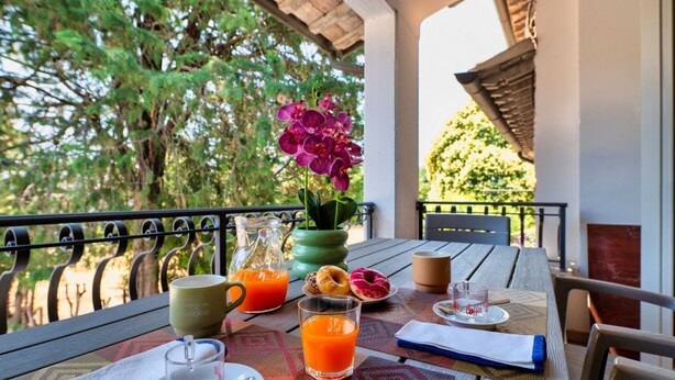 A table with breakfast items, a glass of orange juice, a coffee cup, and a flower vase.