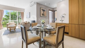 A modern dining area with a glass table, cushioned chairs, and a view of greenery outside.