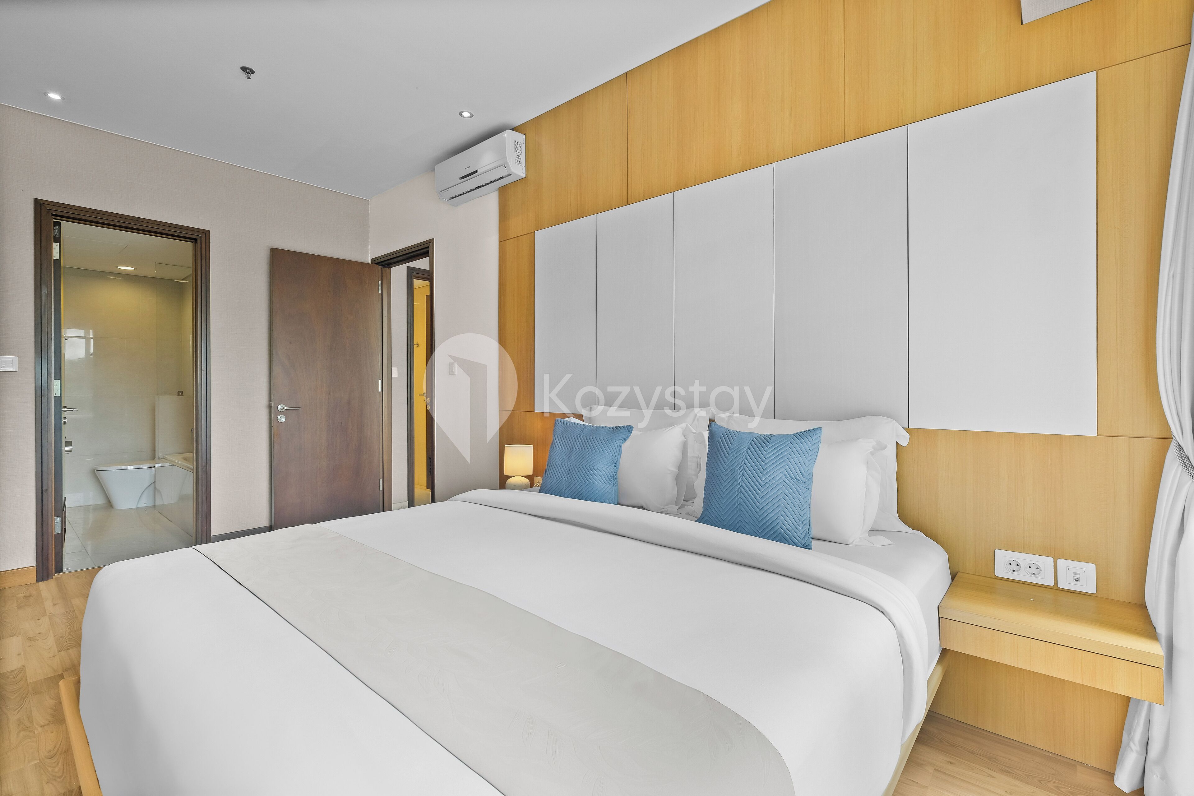 Une chambre d’hôtel moderne avec un grand lit, une tête de lit en bois et une table de chevet avec une lampe.