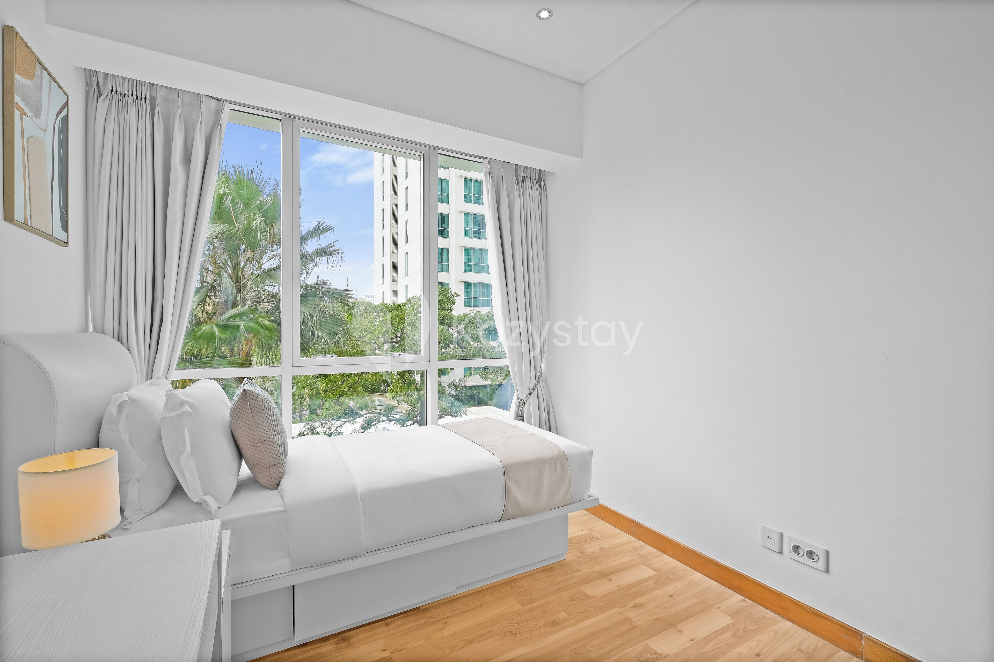 A modern bedroom with a large window, a white sofa, and a bedside table.
