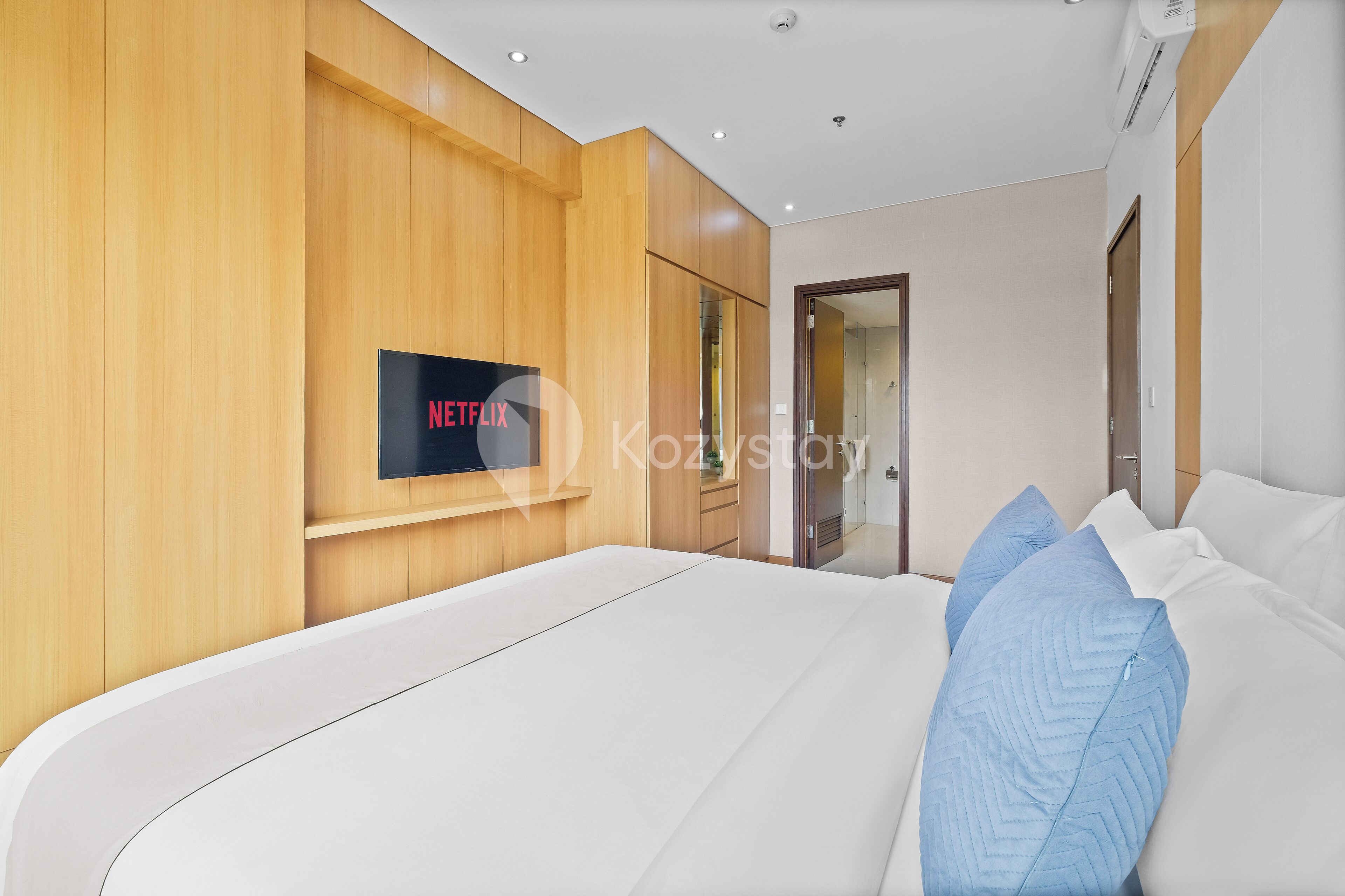 Une chambre d’hôtel moderne dotée d’un grand lit, de lambris en bois, d’un téléviseur fixé au mur et d’une porte donnant accès à une salle de bain.