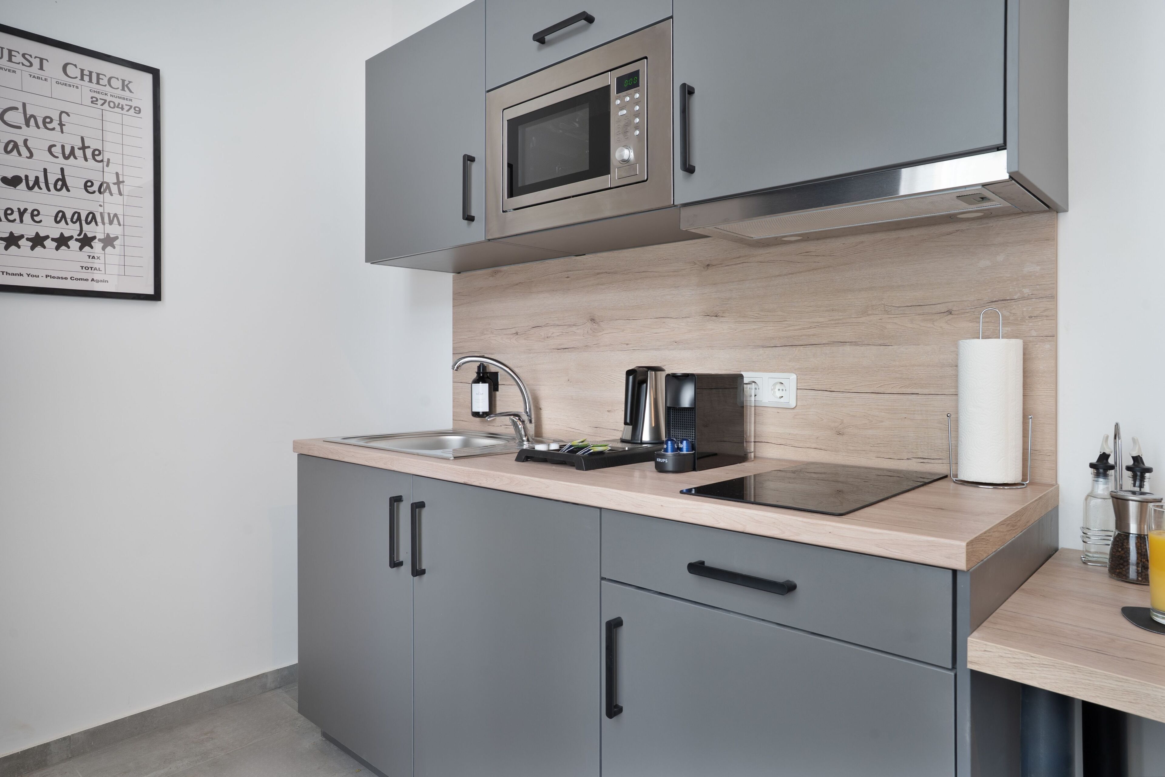 A modern kitchen with grey cabinets, a stainless steel microwave, a coffee machine, and a sink.