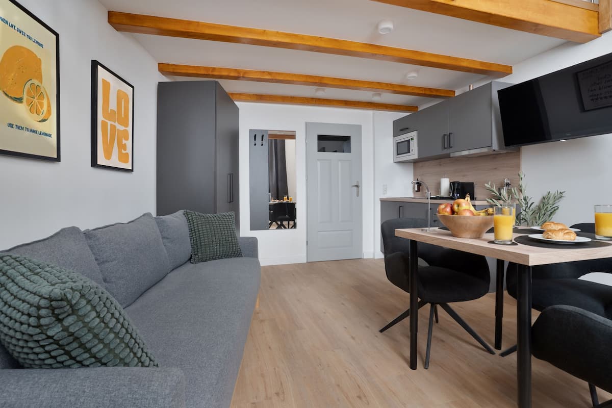 Un salon moderne avec un canapé gris, une table à manger avec des chaises et un coin cuisine doté de meubles gris et d’un téléviseur à écran plat.