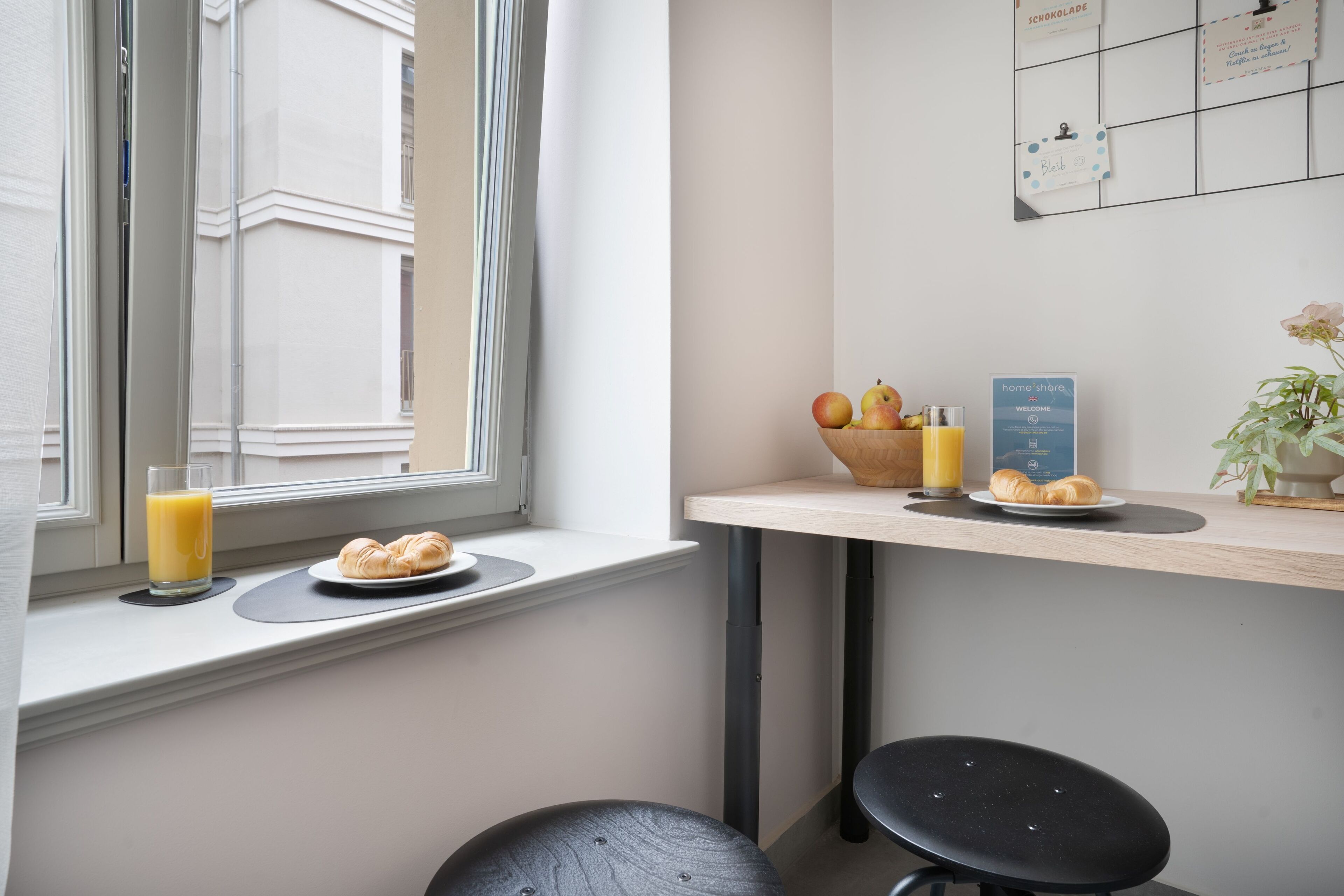 A breakfast setup with croissants, a glass of orange juice, and a bowl of fruit on a window sill.