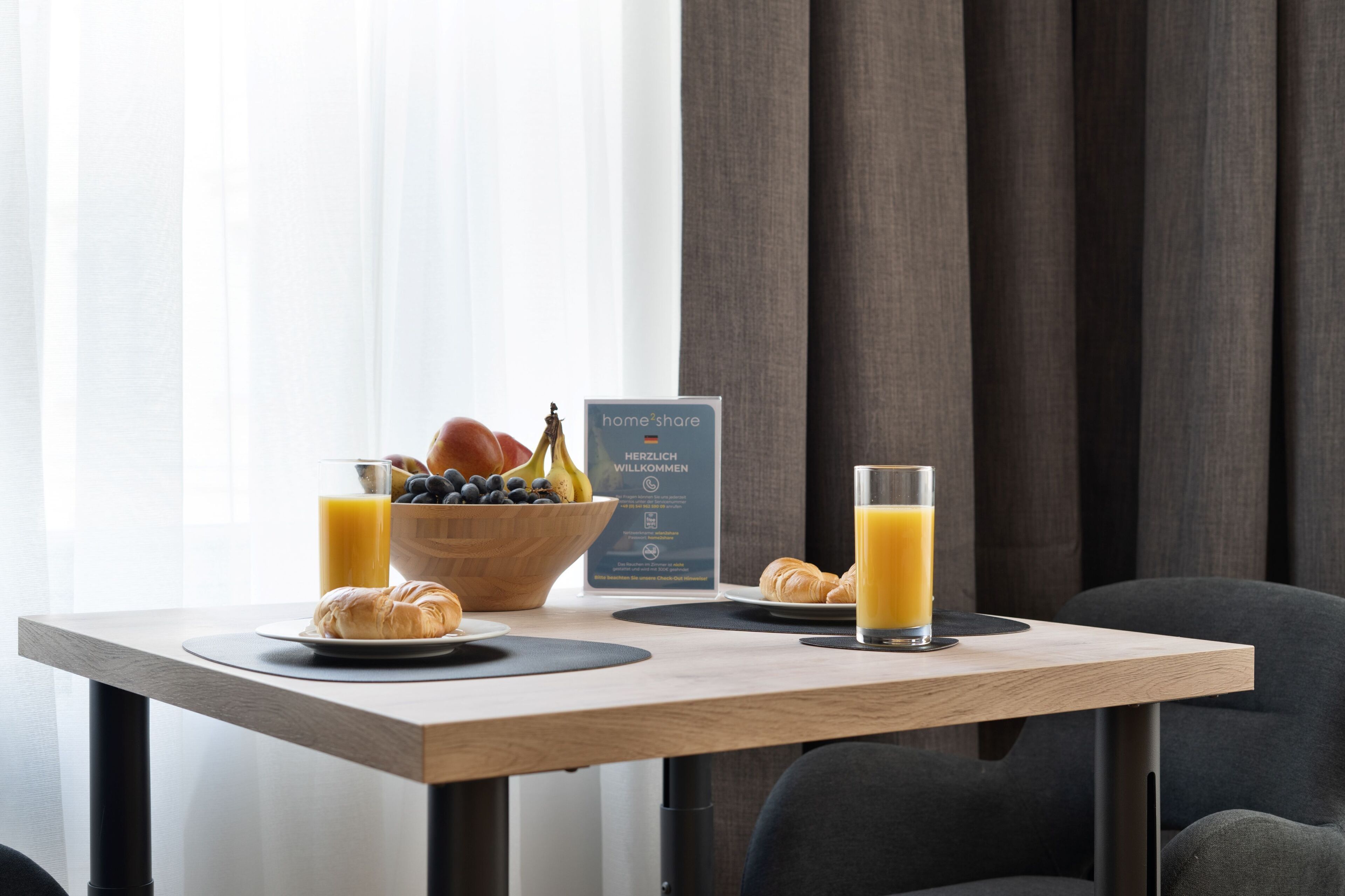 Ein Esstisch mit Croissants, einer Obstschale und einem Glas Orangensaft.