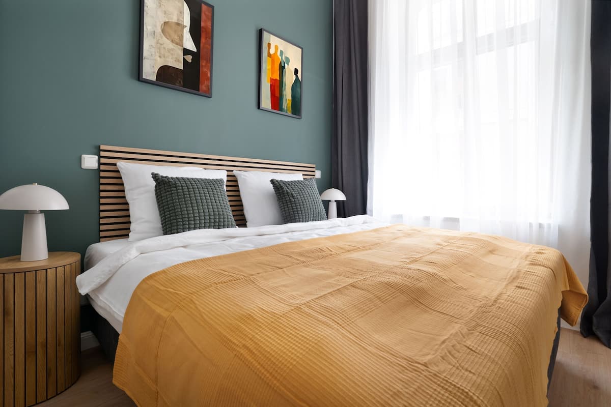 Un lit bien fait, avec une couverture de couleur moutarde, une tête de lit en bois et deux lampes de chevet.