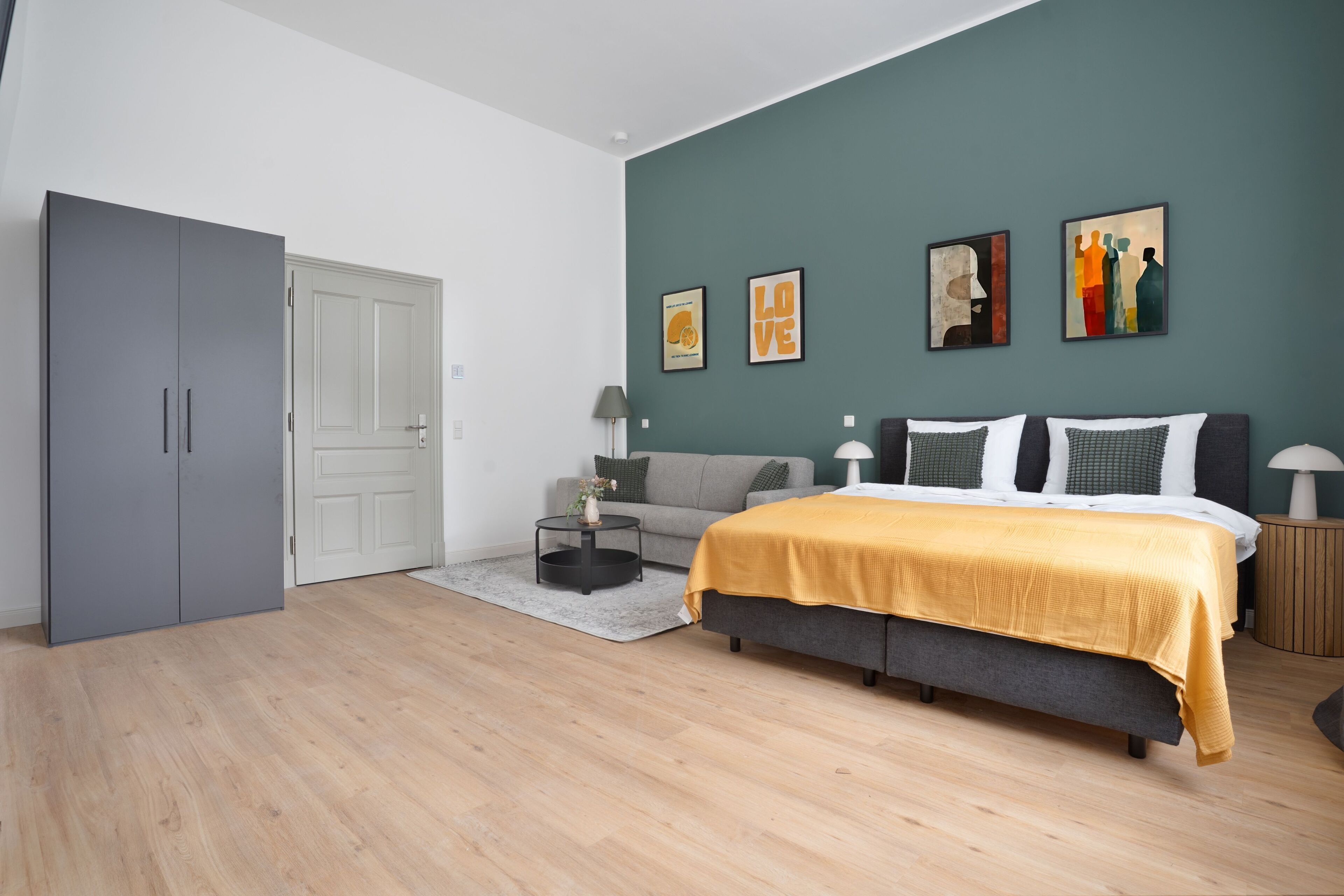 A modern bedroom with a bed, grey wardrobe, and artwork on the wall.