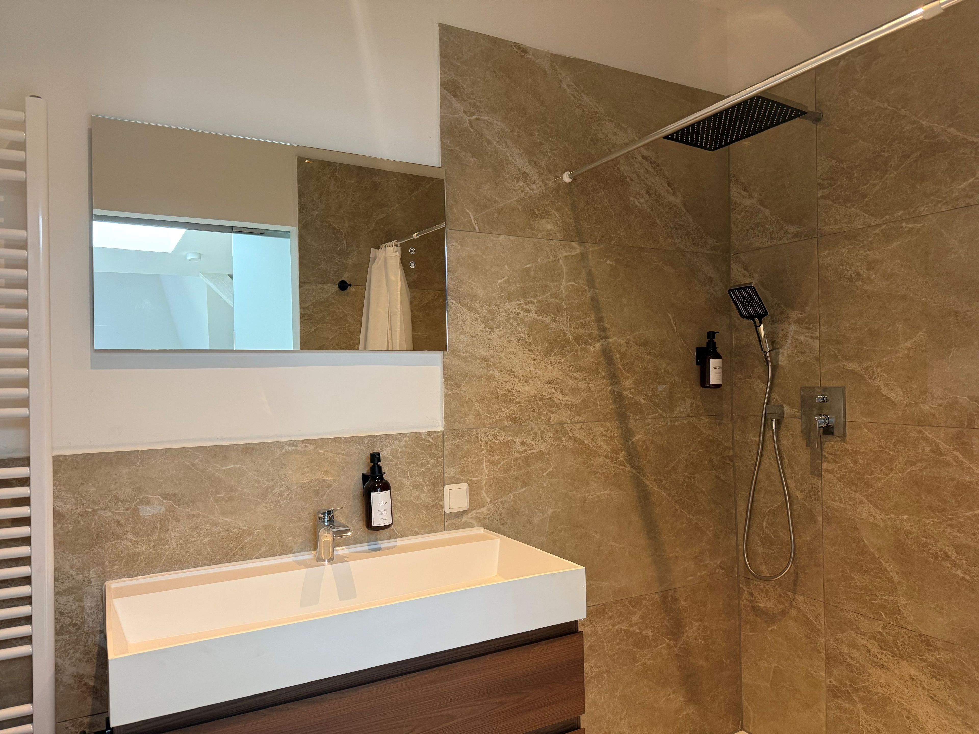 A modern bathroom with a large mirror, a sink, and a shower area.