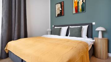 Een net opgemaakt bed met een geel sprei, een grijs hoofdeinde en twee bedlampen.