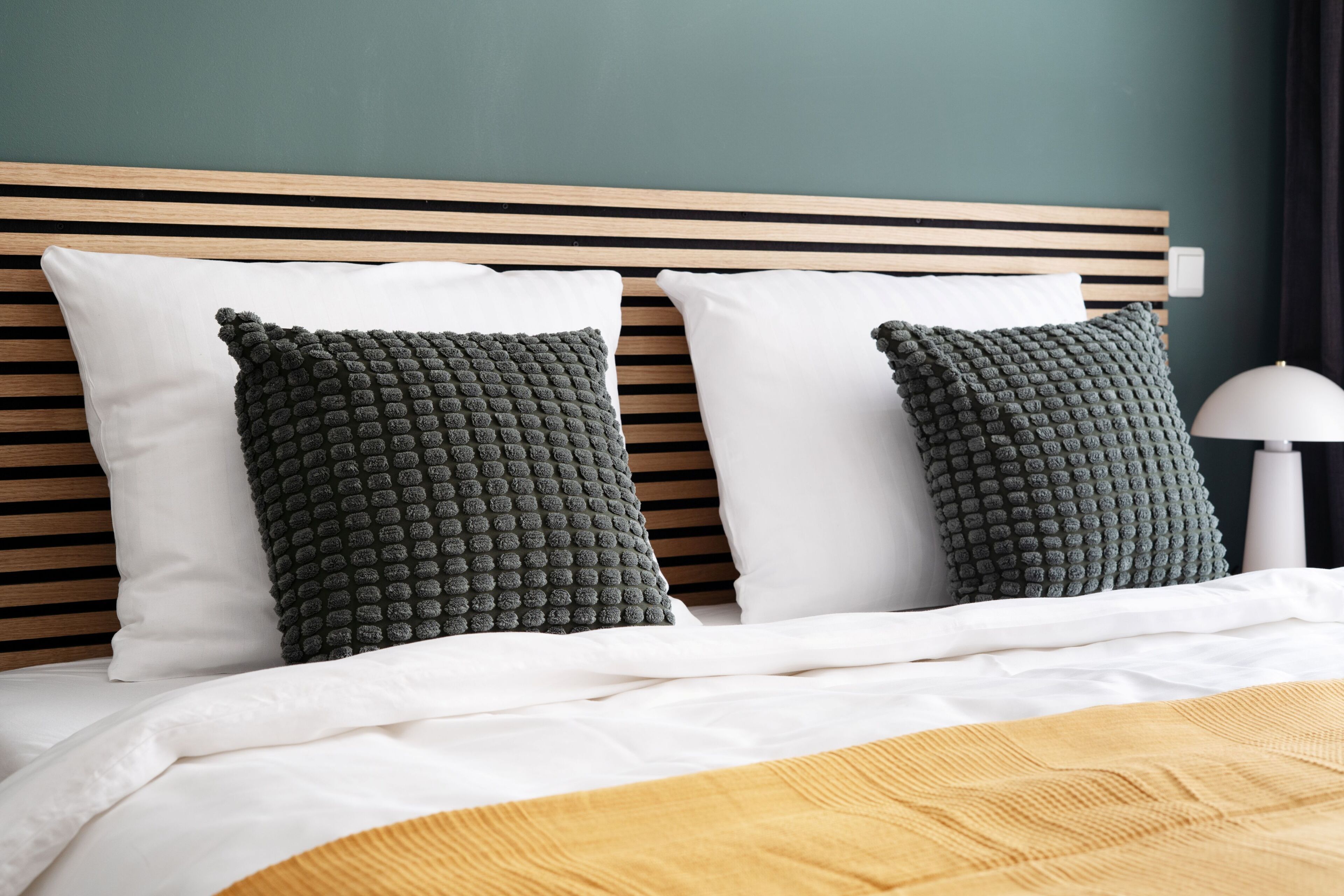 A bed with a wooden headboard, two dark green textured pillows, and a white pillow.