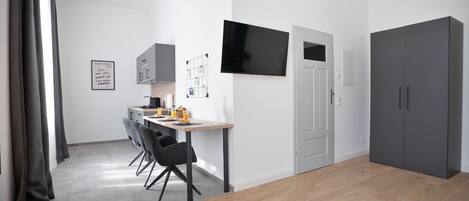 A modern, minimalist room with a dining area, a grey wardrobe, and a flat-screen TV mounted on the wall.