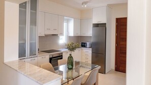Una cocina moderna con armarios blancos, un refrigerador de acero inoxidable, una mesa de comedor de vidrio y un jarrón con flores.
