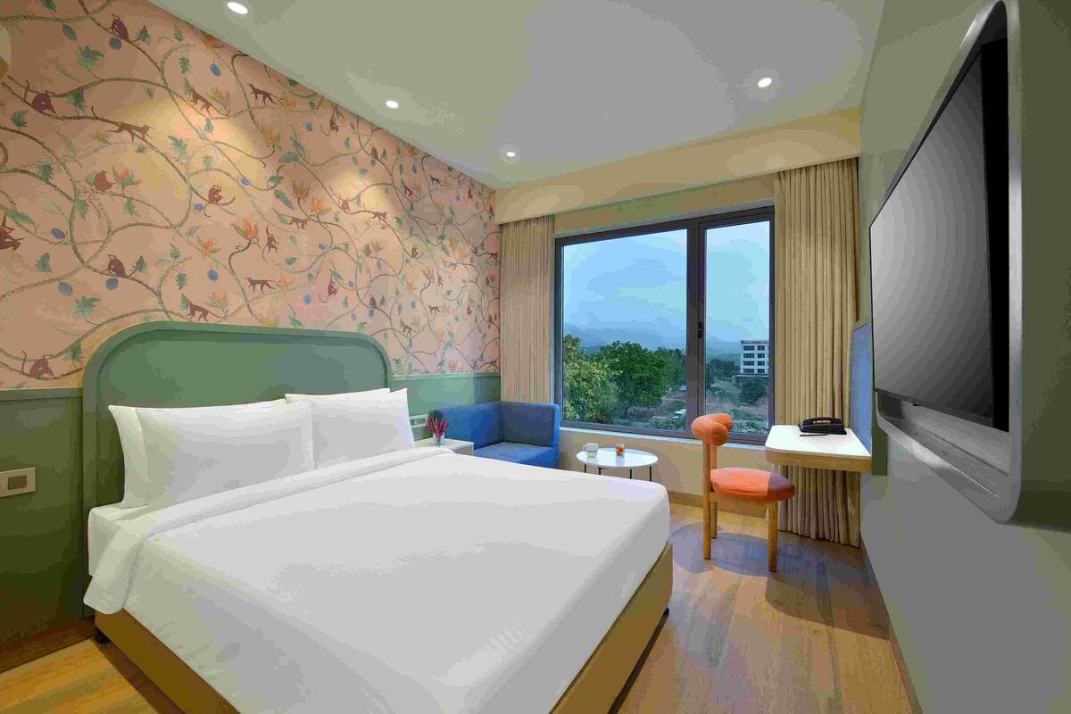 Una habitación de hotel con una cama grande, un sillón azul, una mesita redonda y un televisor.